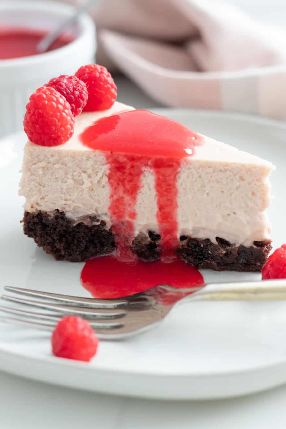 close up of slice of raspberry brownie cheesecake on a white plate