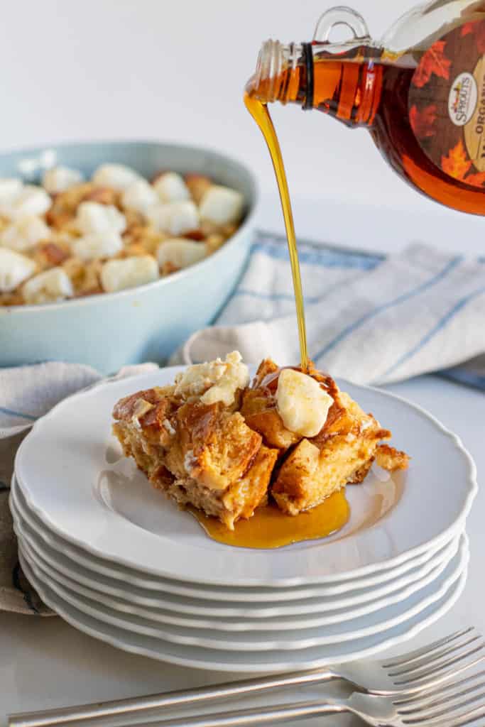 a slice of apple french toast casserole on stack of plates with maple syrup poured over top