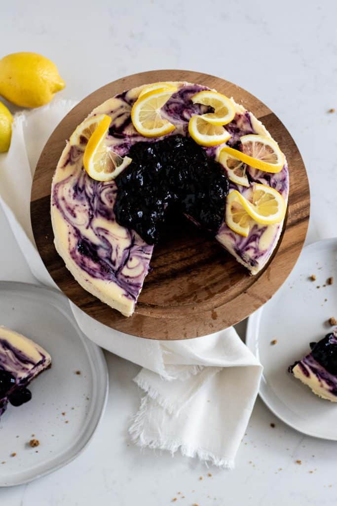 overhead view of whole lemon blueberry cheesecake and slices on a plate