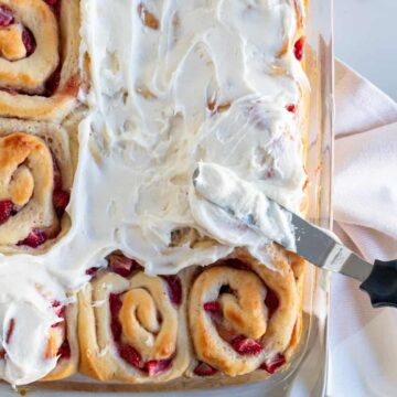 pan of strawberry rolls being frosted with cream cheese frosting