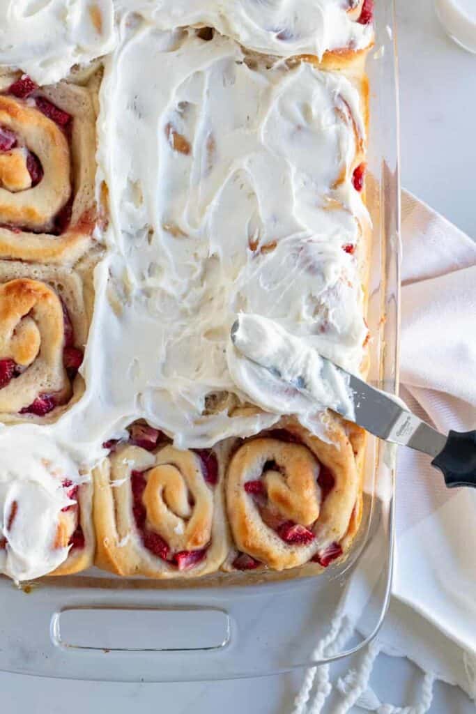 pan of strawberry rolls being frosted with cream cheese frosting