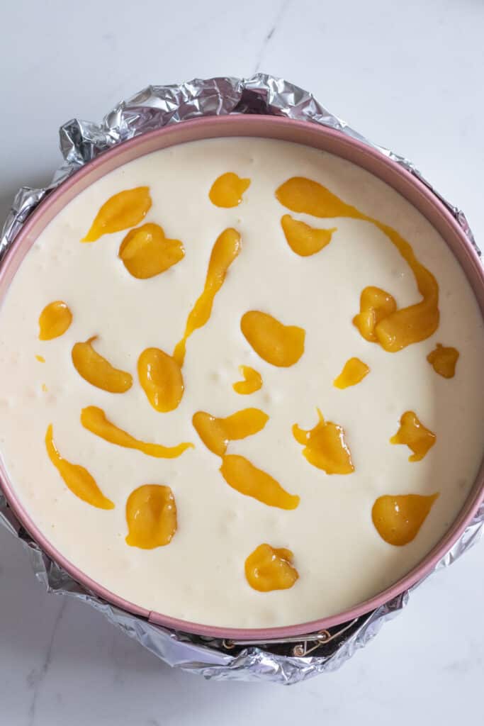 unbaked cheesecake in pan with dollops of mango puree