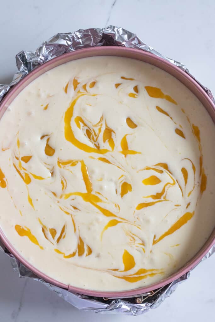 unbaked cheesecake in pan with swirls of mango puree