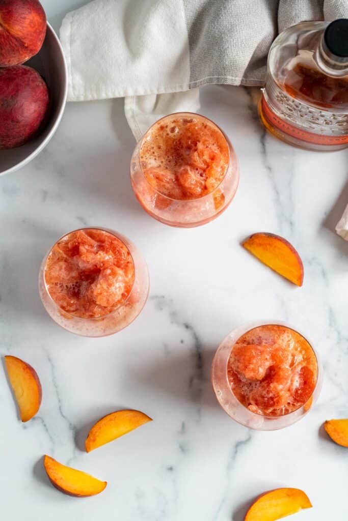 overhead view of 3 glasses of peach bourbon slush on marble counter