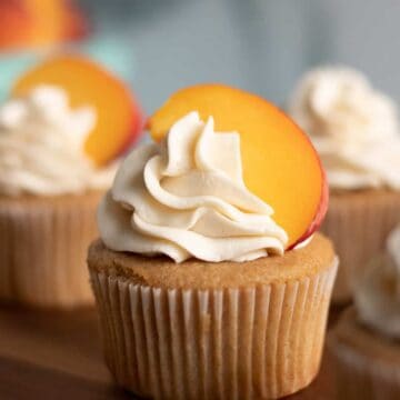 Peach cobbler cupcake with a fresh peach on top on a wood serving platter