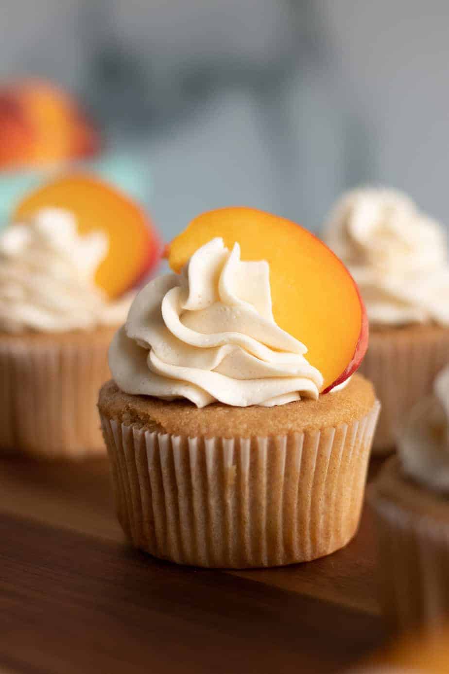 Peach cobbler cupcake with a fresh peach on top on a wood serving platter