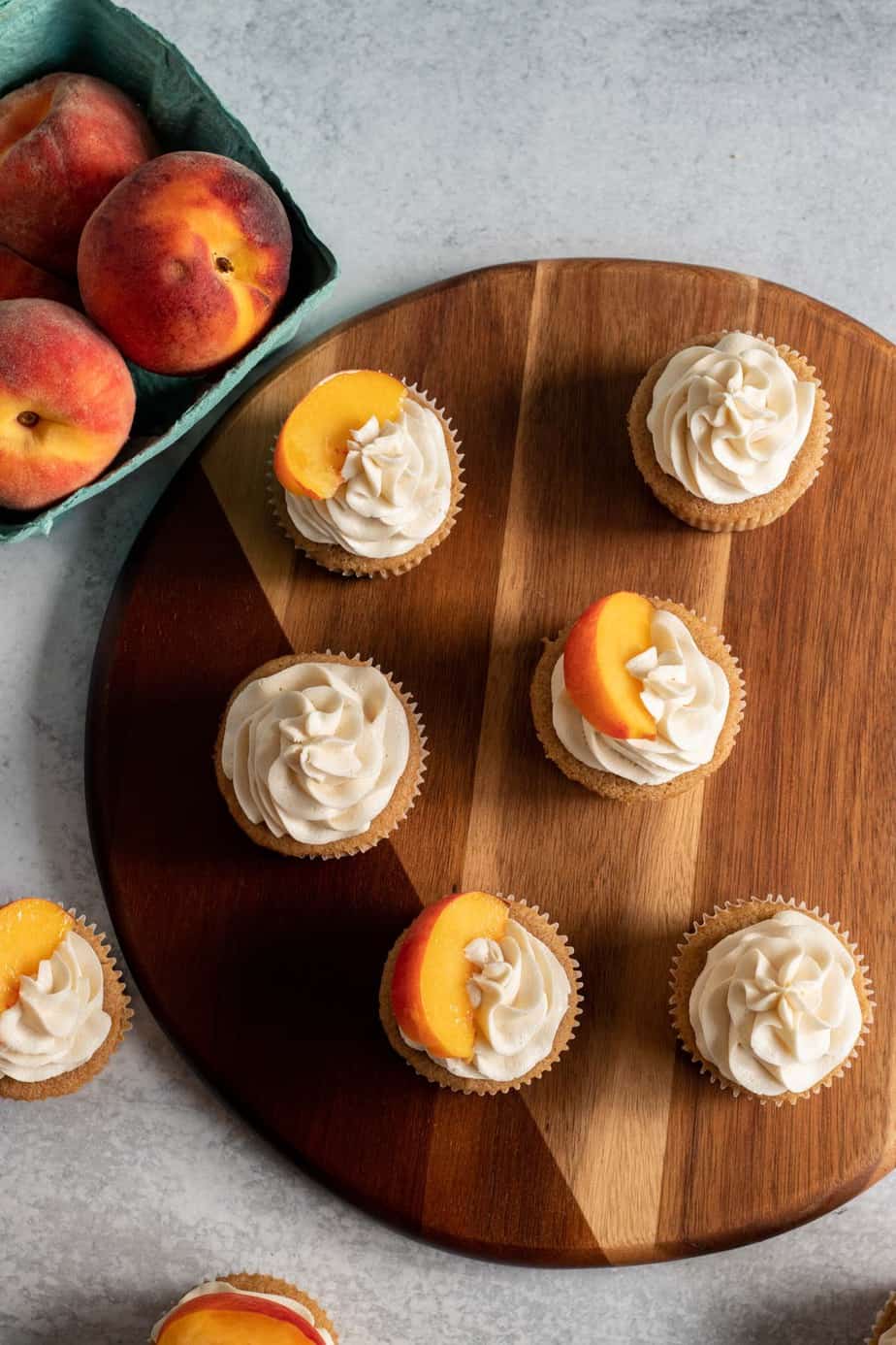 overhead view of cupcakes with vanilla frosting and peach slices on top on a wooden board