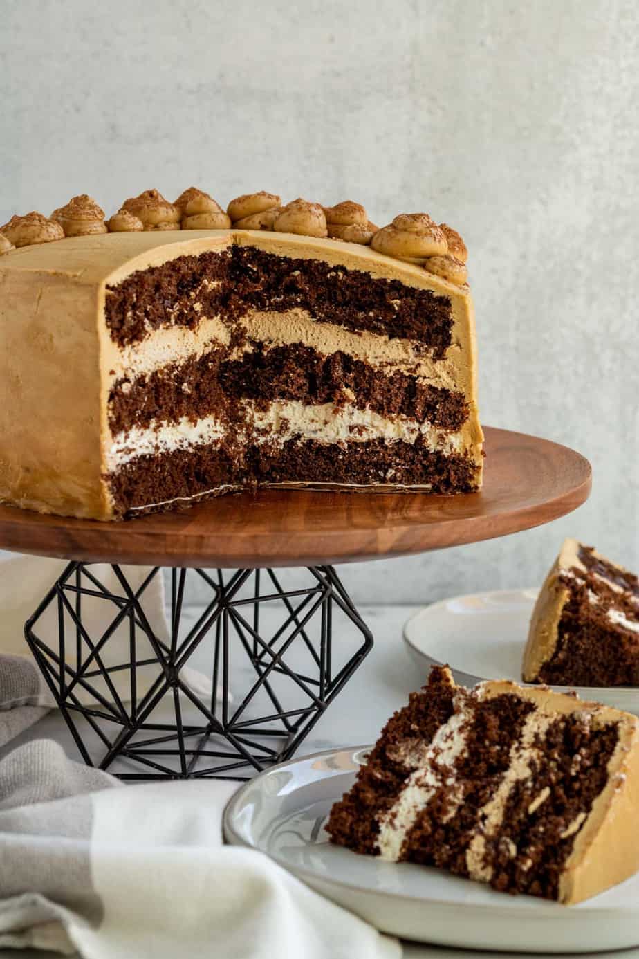 chocolate mocha cake cut open sitting on black metal and wood cake stand with 2 slices of cake on plate