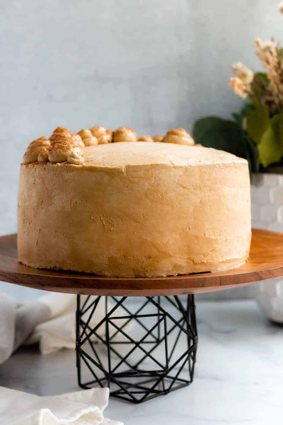 chocolate mocha cake on a wood and black metal cake stand with a white vase of flowers