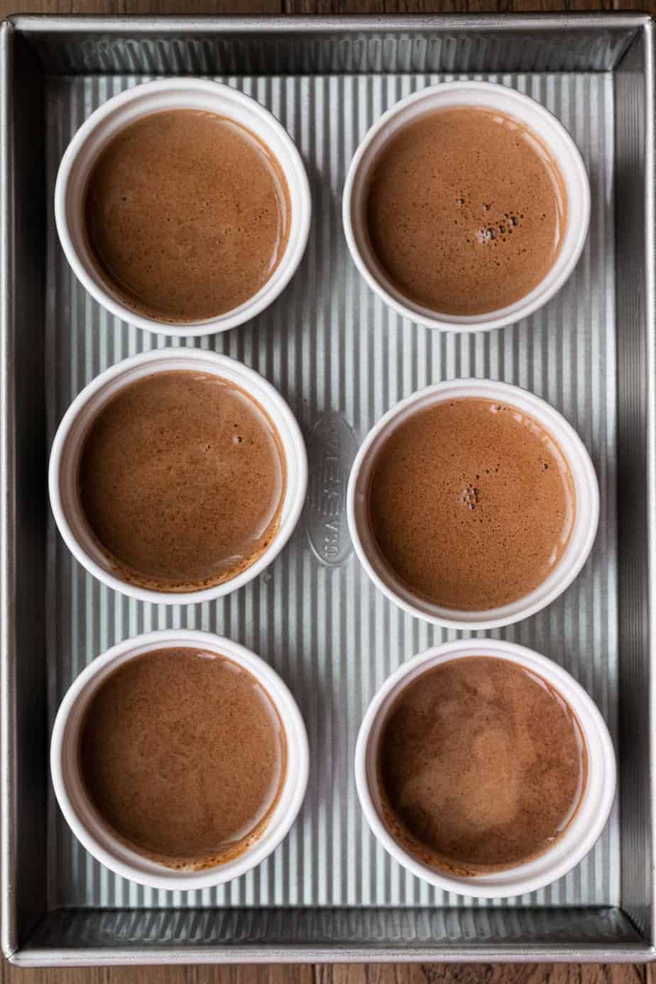 6 white ramekins with unbaked chocolate pot de creme in baking pan 