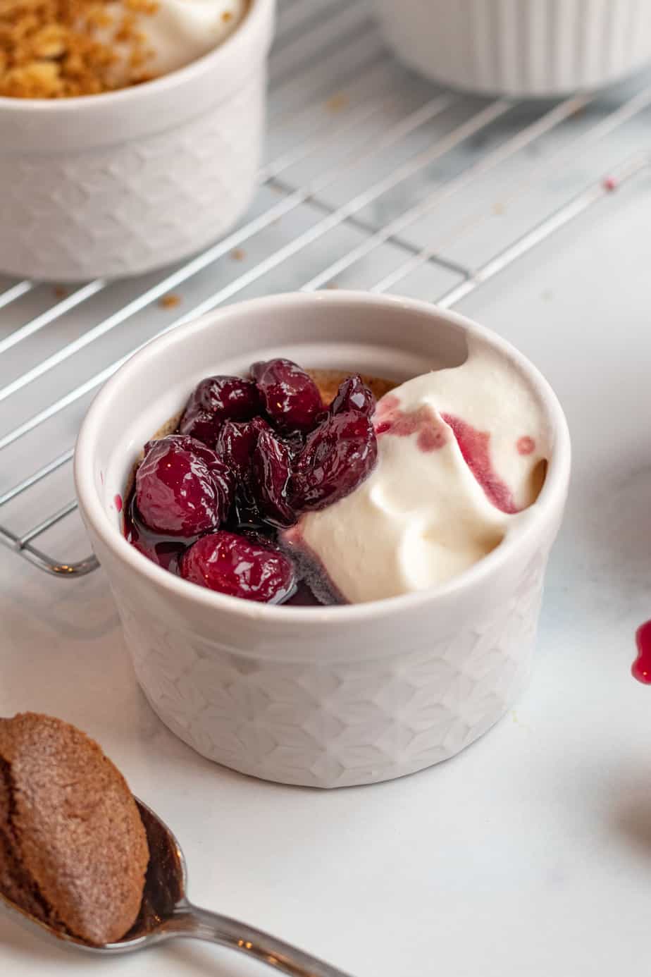 chocolate pots de creme with cherries on top in foreground and pretzel crumble on top in background