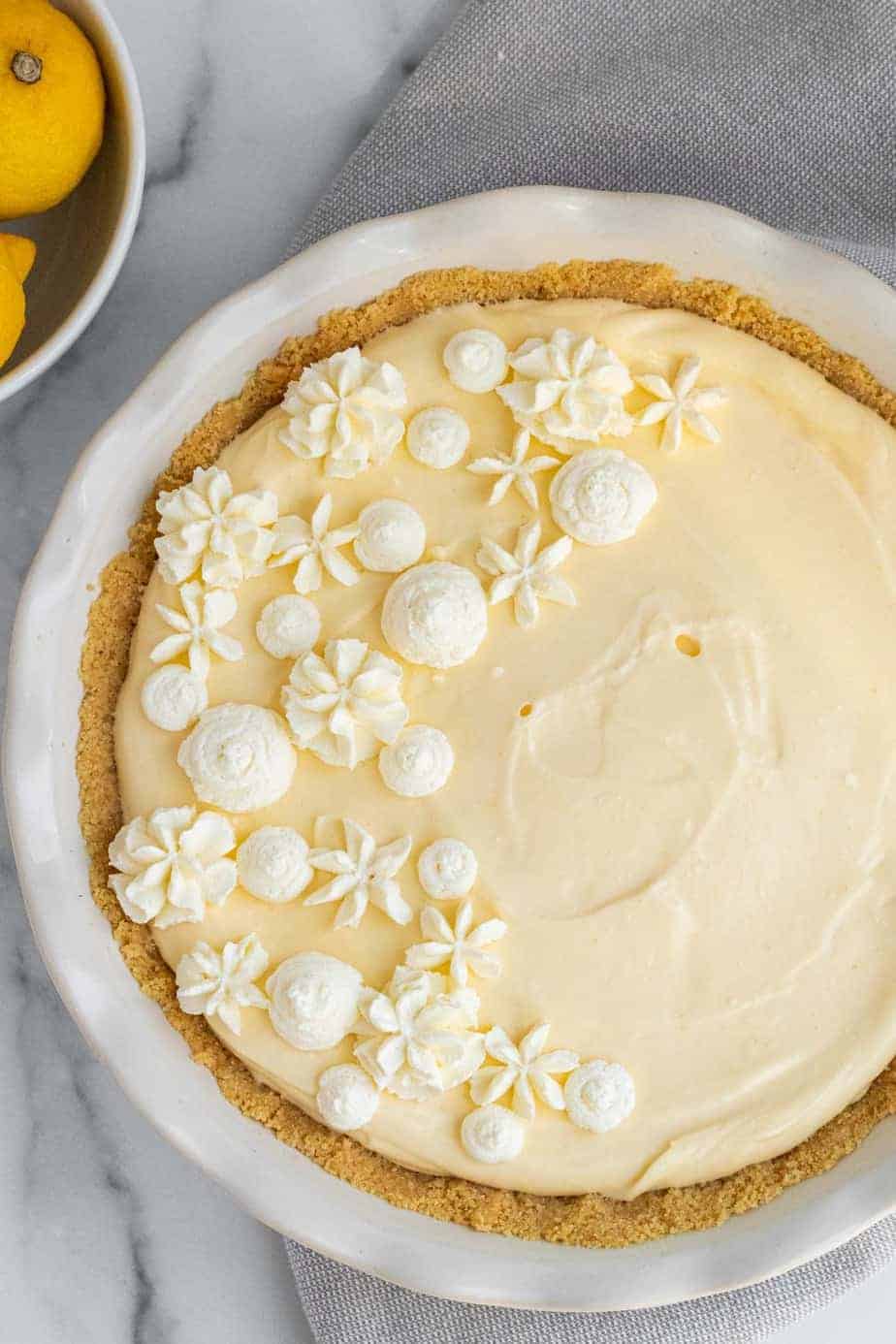 lemon cream pie in a white pie dish next to bowl of lemons