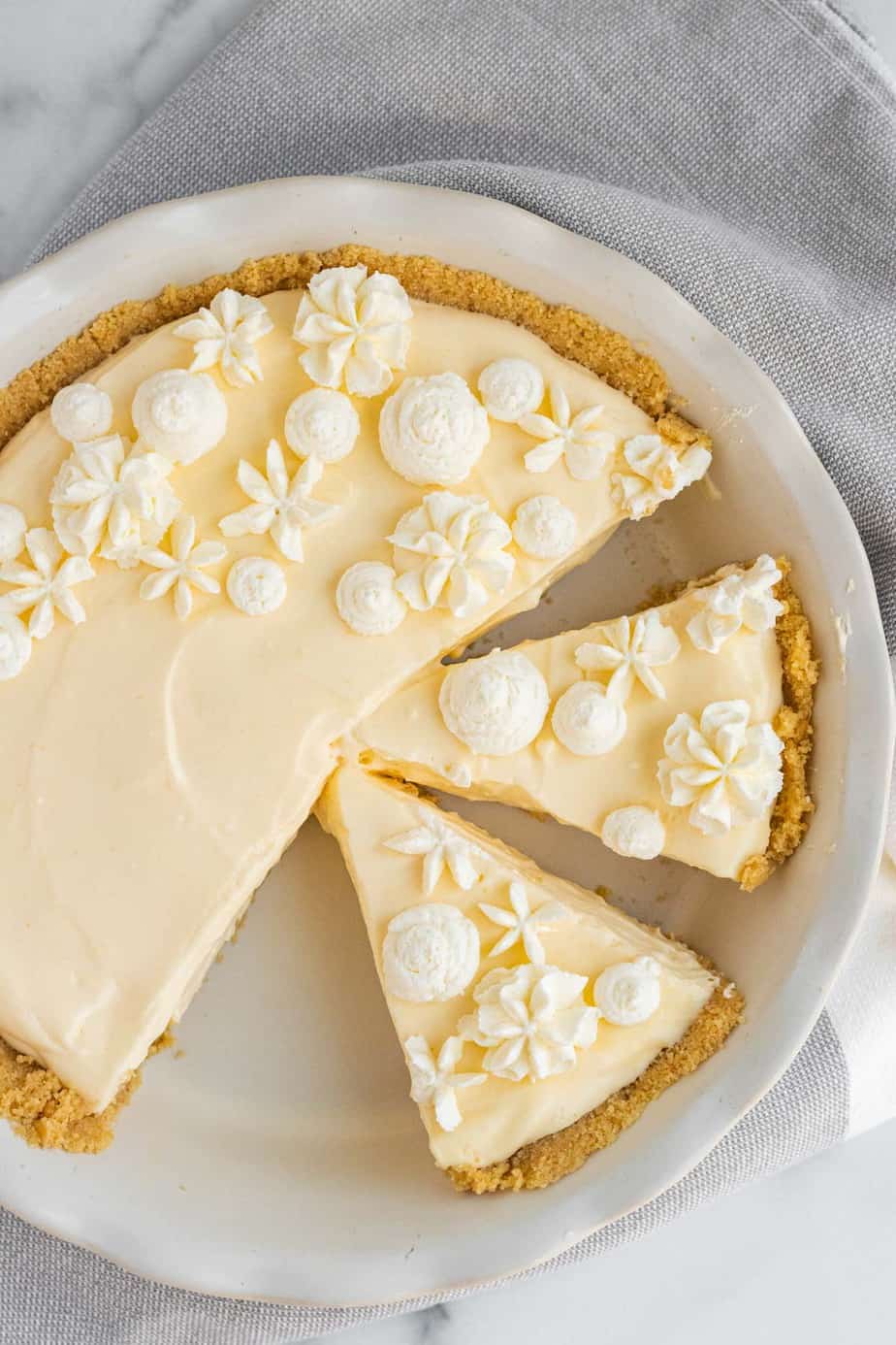 lemon cream pie with whipped cream decorations in white pie dish with 2 slices cut from pie