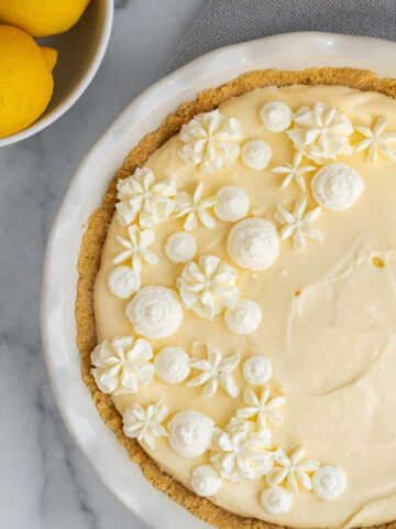 lemon cream pie in a white pie dish next to bowl of lemons