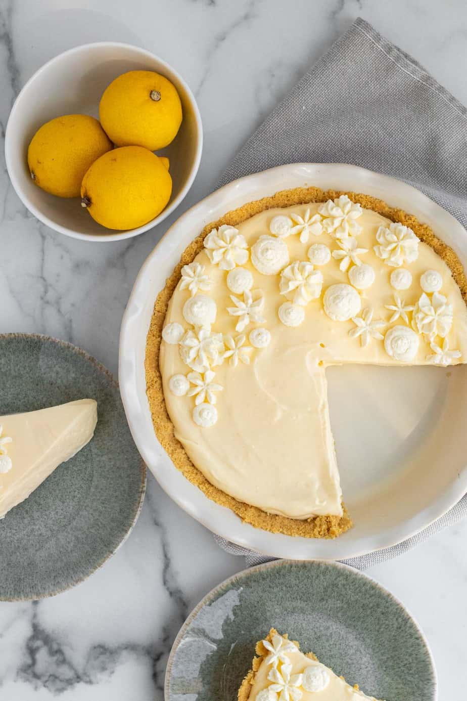 2 slices of lemon pie on green plates with bowl of lemons and pie dish 