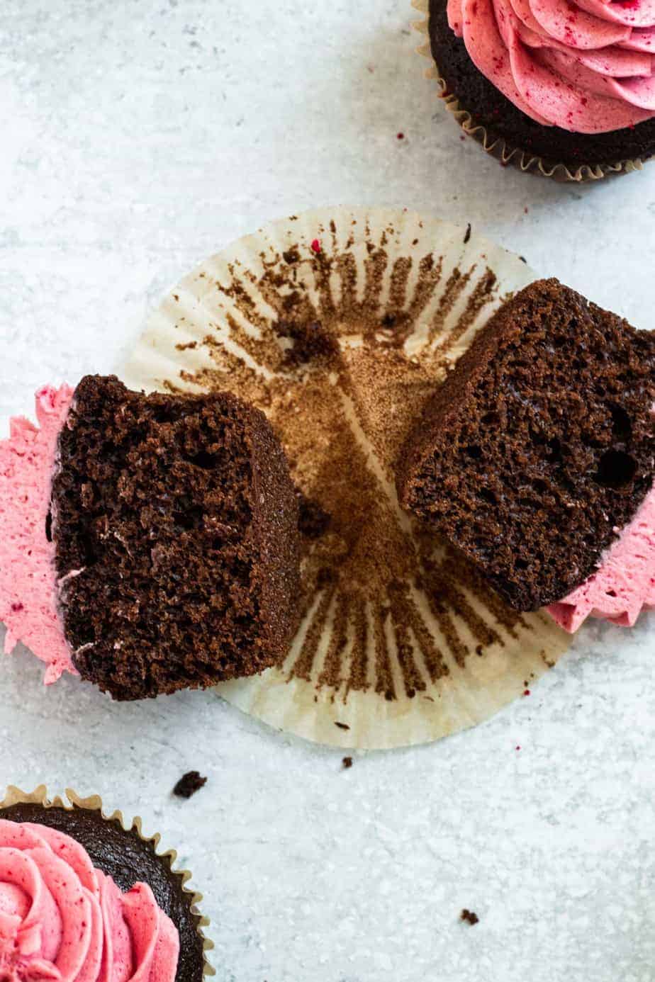 chocolate raspberry cupcake cut in half lying on a paper wrapper