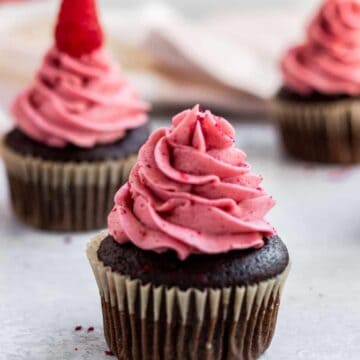 chocolate cupcakes with raspberry buttercream and a pink glass cake stand in the back