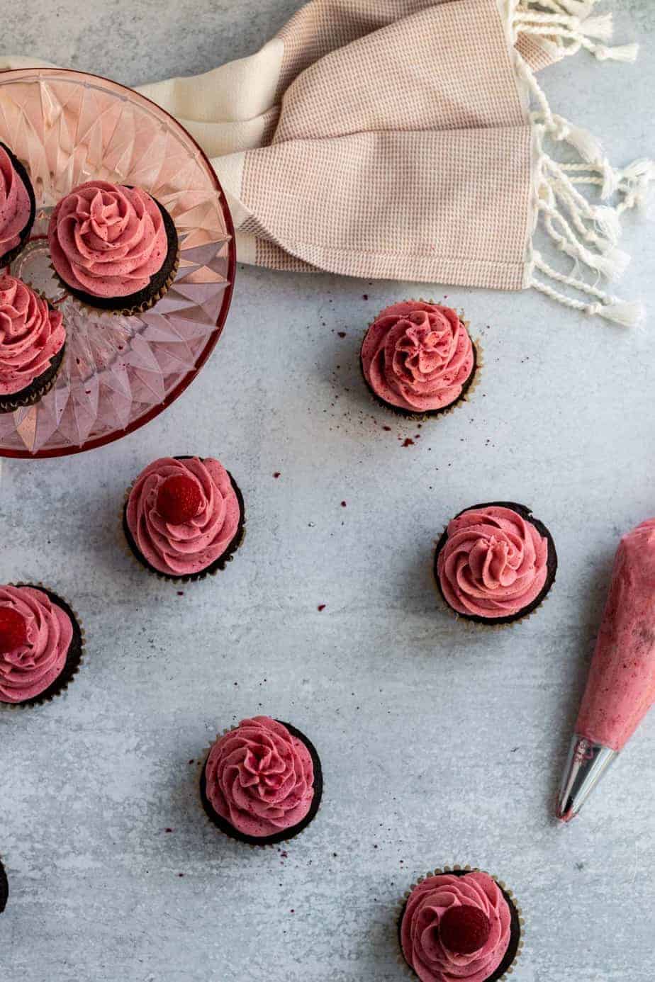 overhead view of chocolate raspberry cupcakes on a table with a piping bag of raspberry buttercream
