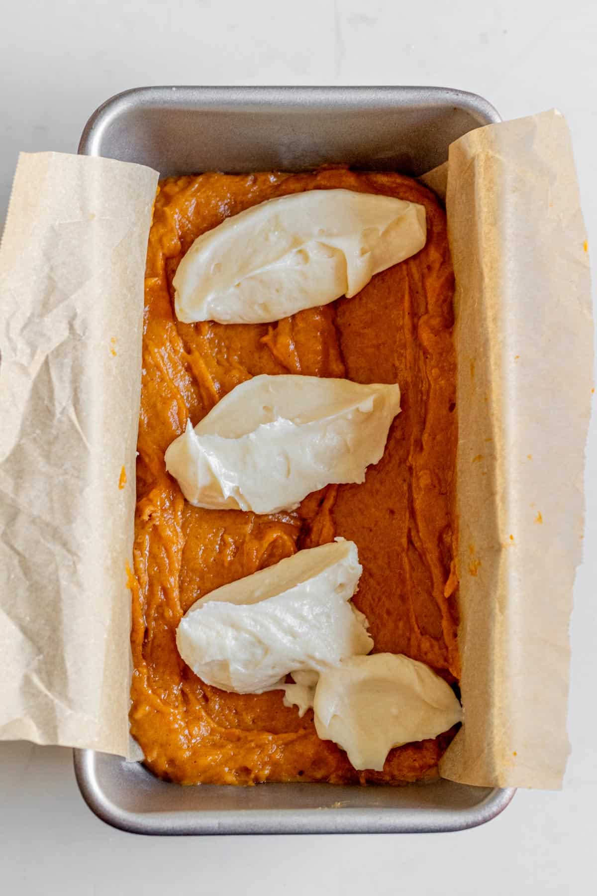 dollops of cream cheese on top of pumpkin bread batter in a loaf pan