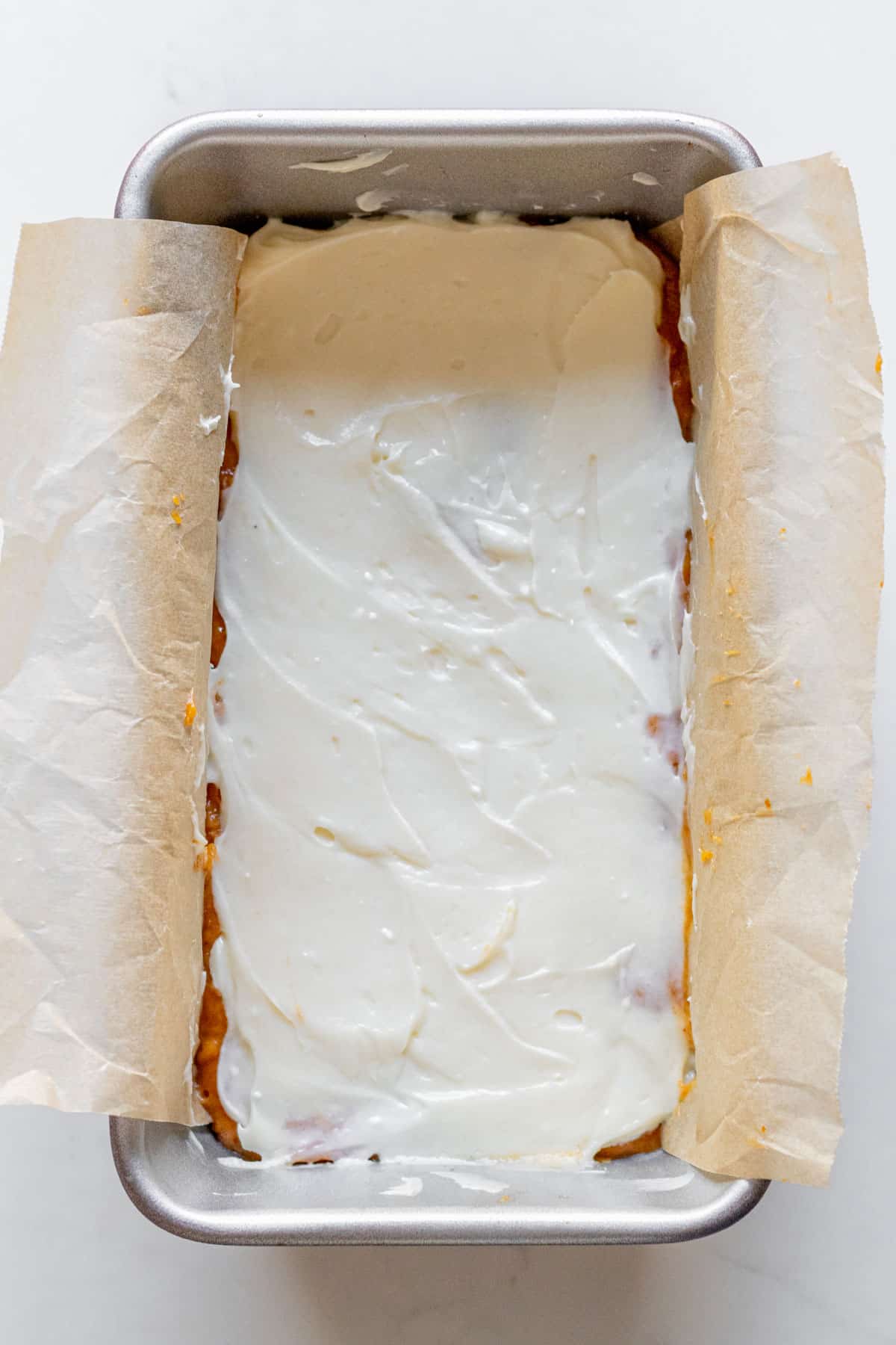 cream cheese spread over pumpkin bread batter in a loaft pan