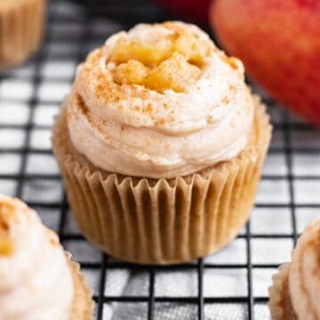 cupcake with frosting and apple pie filling on top sitting on black wire cooling rack