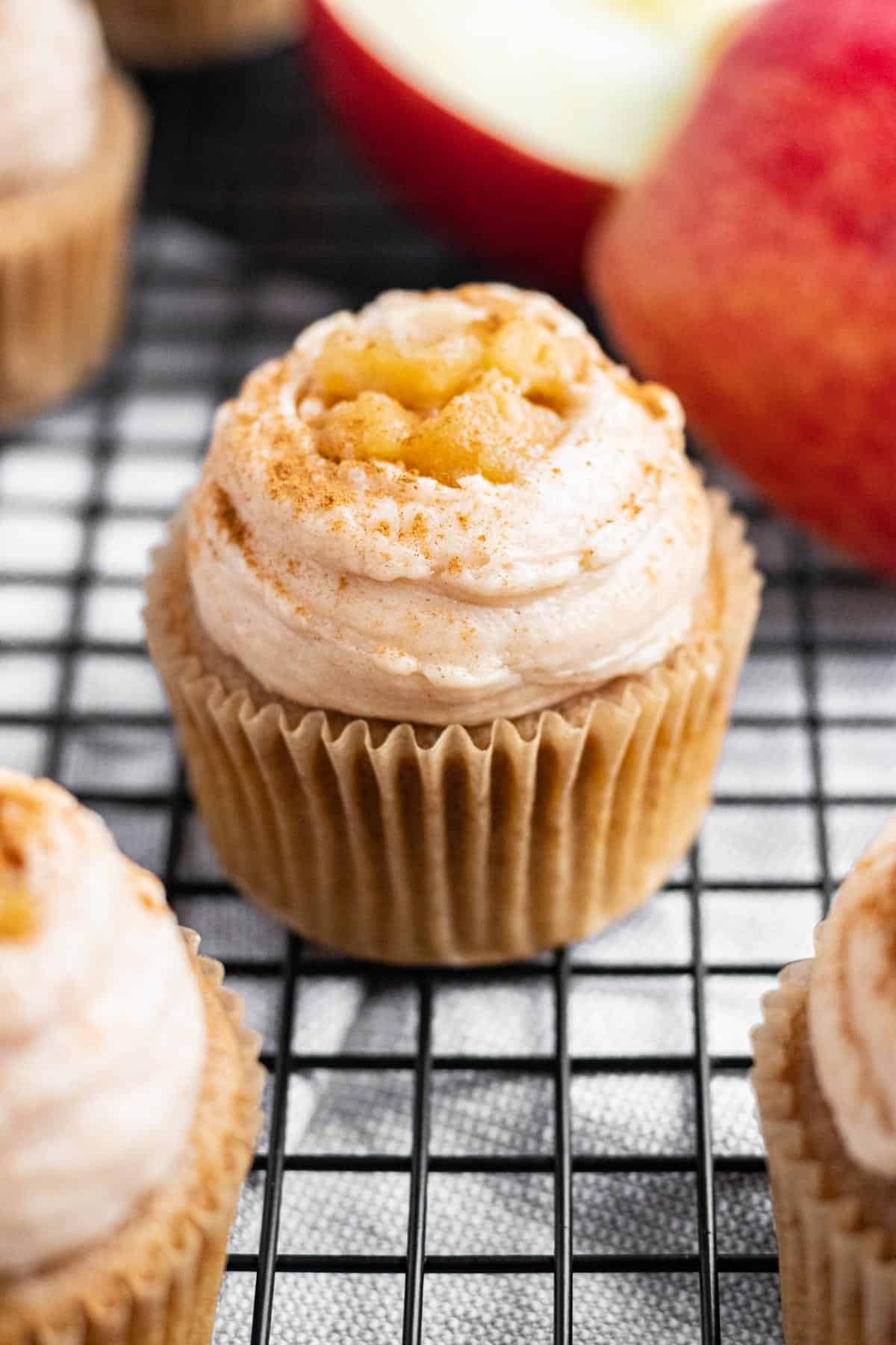 cupcake with frosting and apple pie filling on top sitting on black wire cooling rack