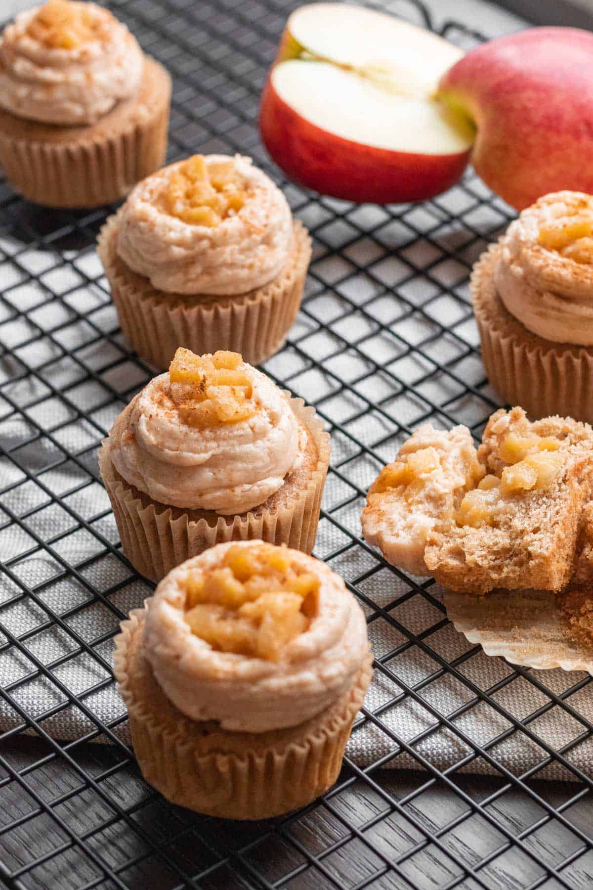 apple pie cupcakes with apple pie filling on top sitting on a wire cooling rack with apple in background