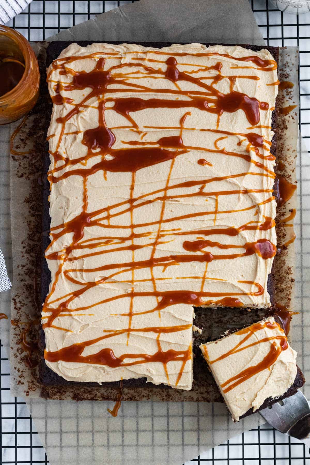 full chocolate sheet cake on a cooling rack with one slice cut. Cake topped with salted caramel buttercream and drizzled with salted caramel.