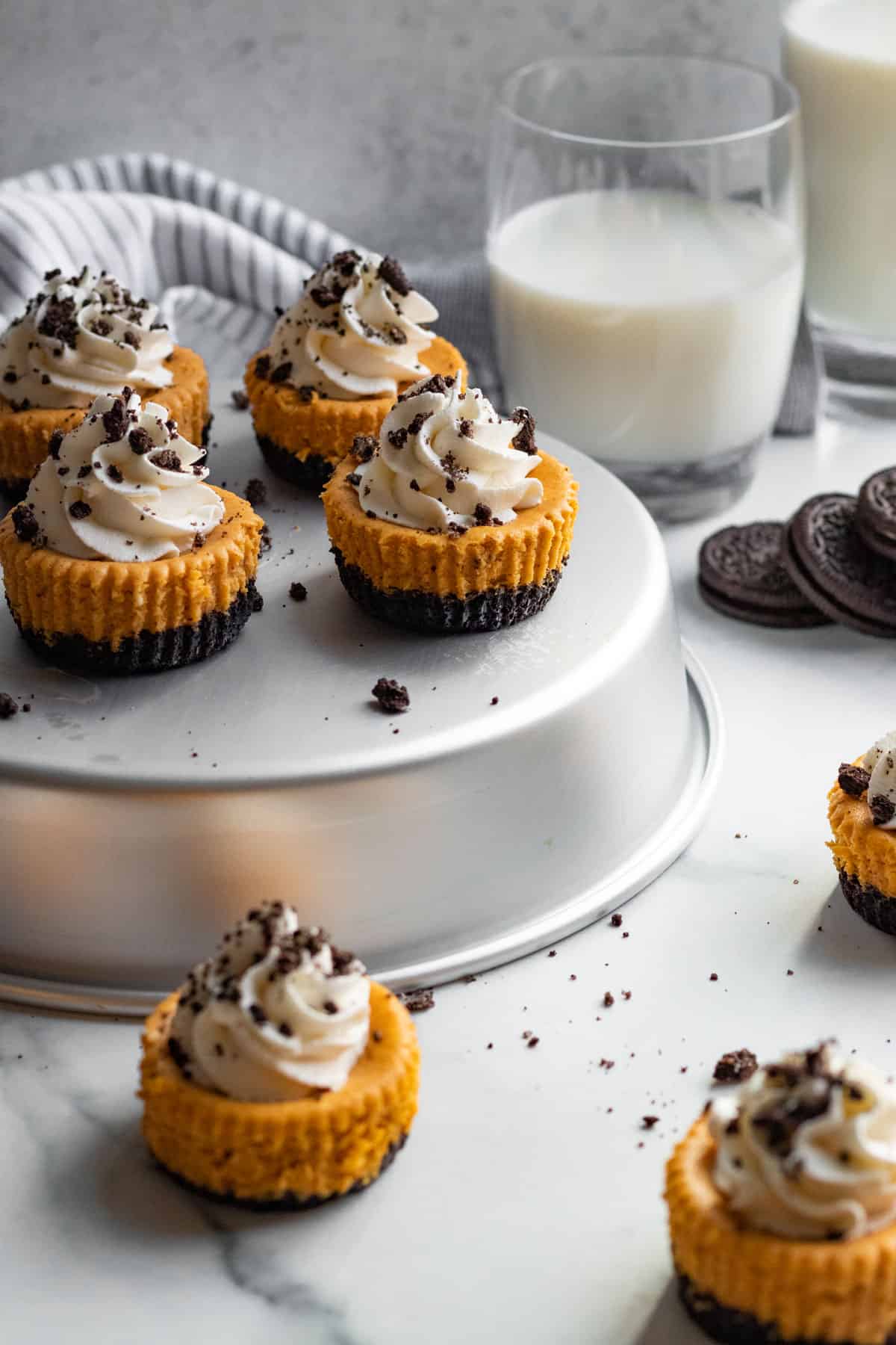 mini pumpkin cheesecakes with whipped cream sitting on silver tin with cookies and milk in the background