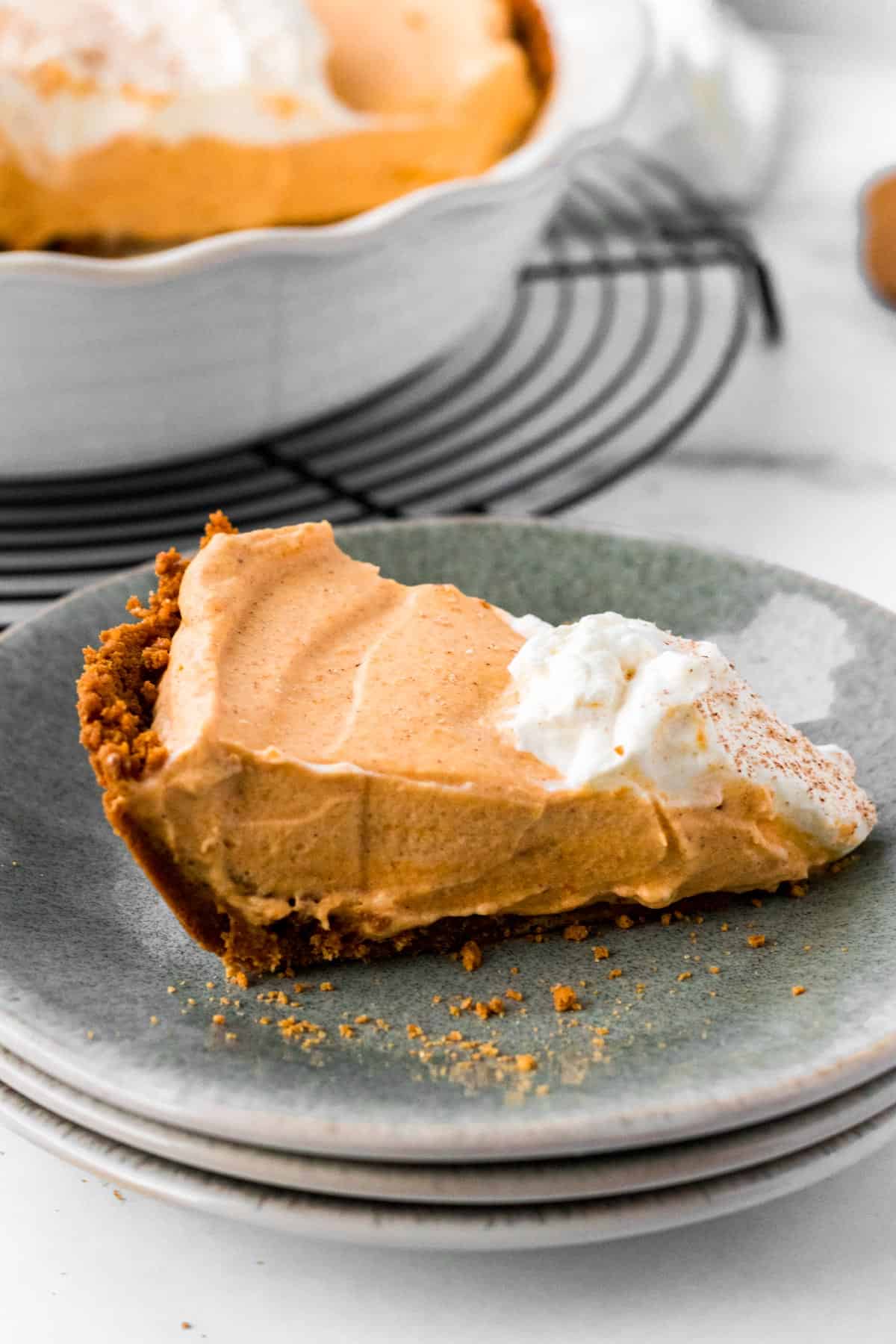 slice of pumpkin mousse pie on stack of plates with full pie in background