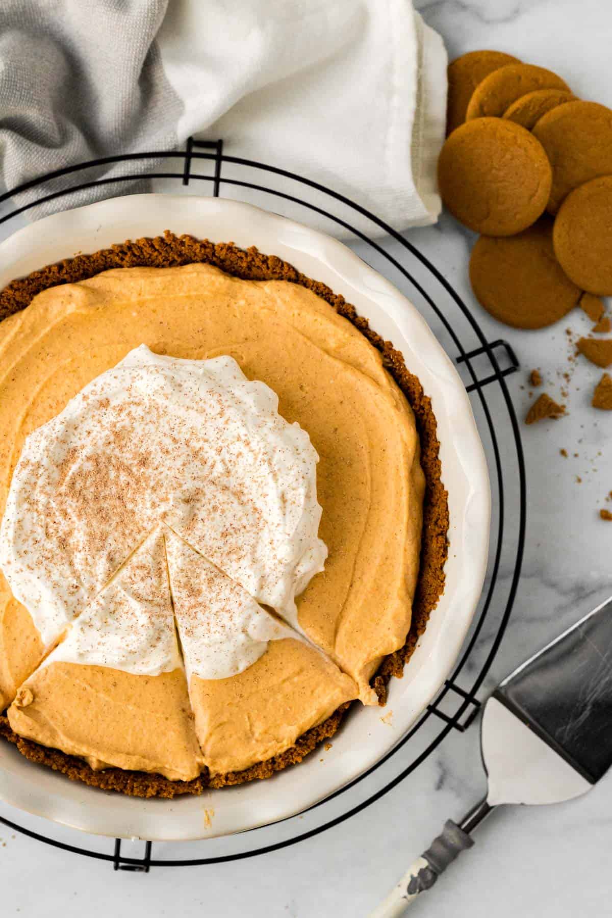 pumpkin mousse pie in white pie dish on black cooling rack with pie server and gingersnap cookies