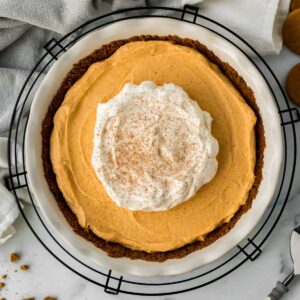 pumpkin mousse pie in white pie dish on black cooling rack with pie server and gingersnap cookies