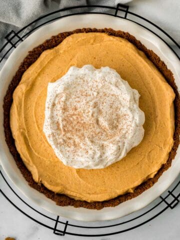 pumpkin mousse pie in white pie dish on black cooling rack with pie server and gingersnap cookies