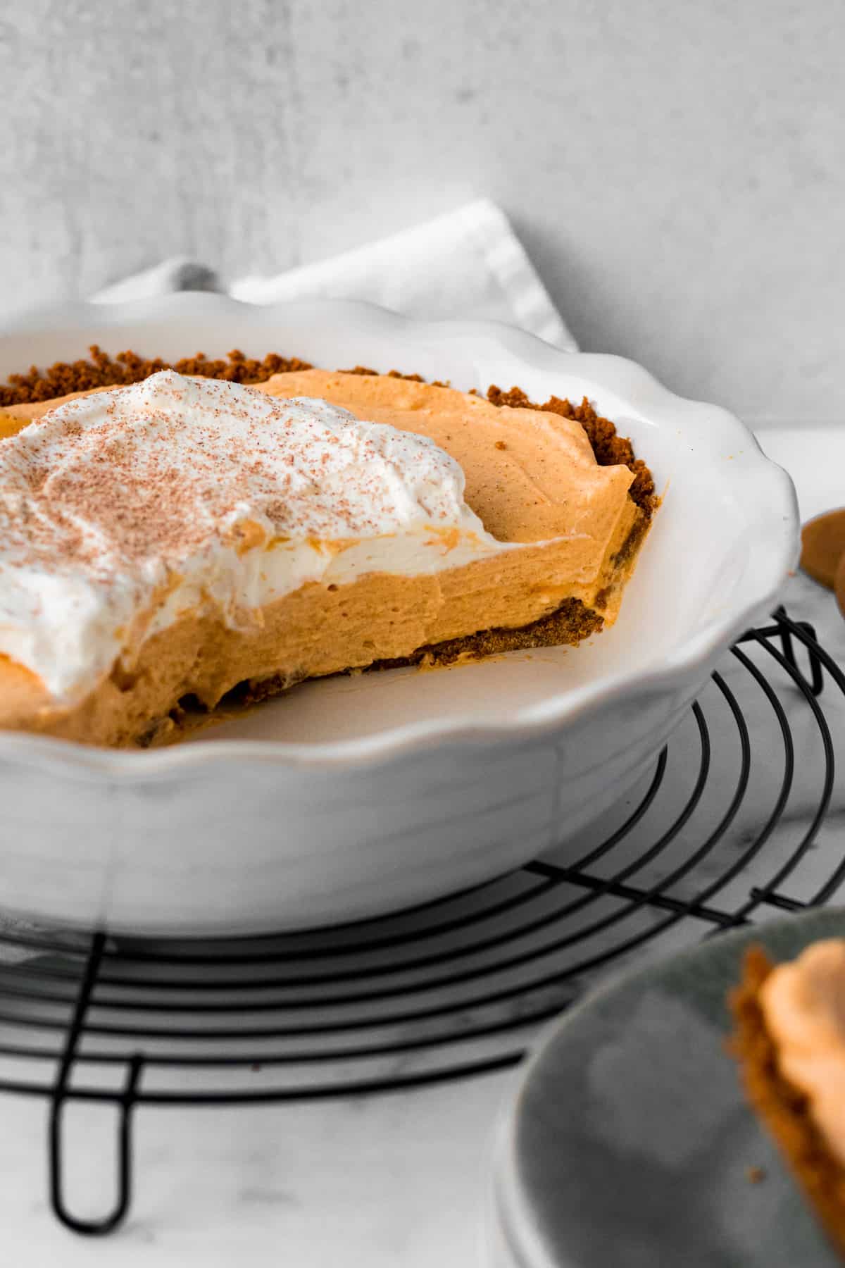 white pie dish on circular cooling rack with half a pumpkin mousse pie inside