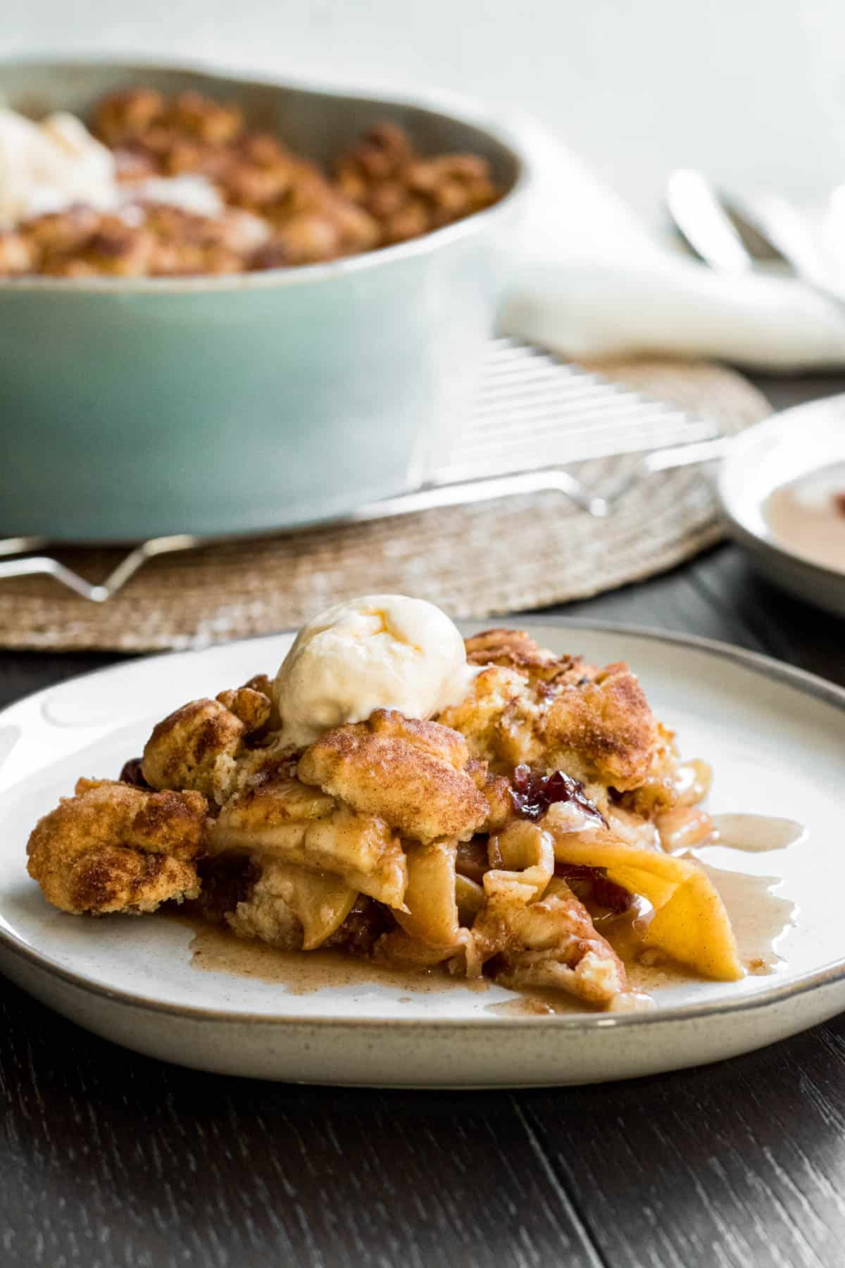 plate of apple crisp with blue baking dish of apple crisp in back ground