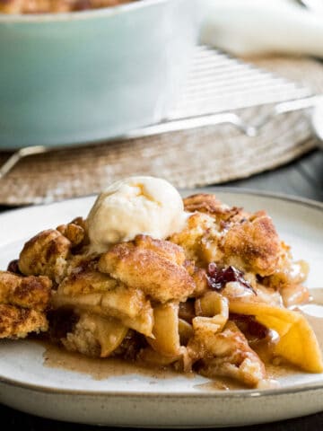 plate of apple crisp with blue baking dish of apple crisp in background