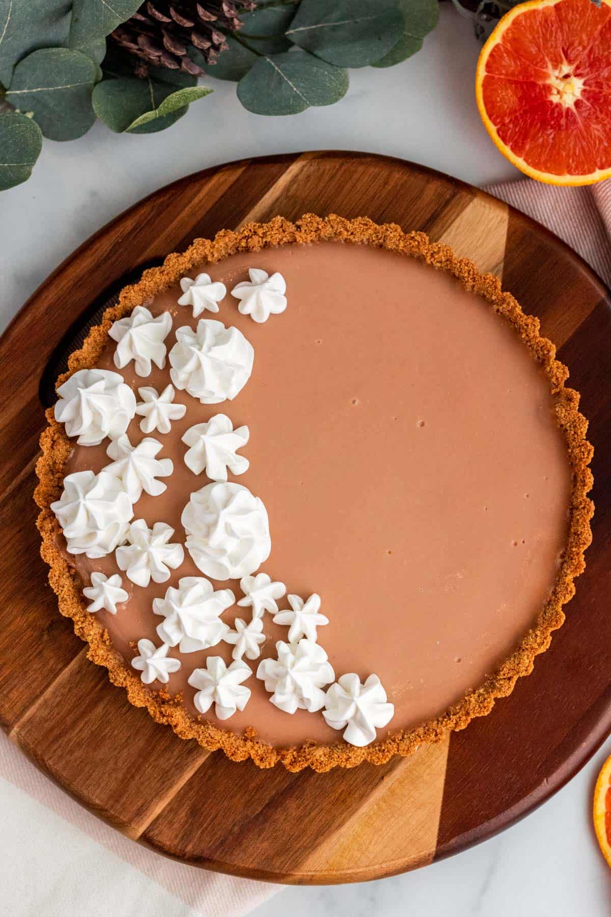 blood orange tart with meringue on a wood platter with oranges around it