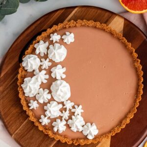 blood orange tart with meringue on a wood platter with oranges around it