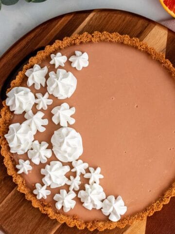 blood orange tart with meringue on a wood platter with oranges around it