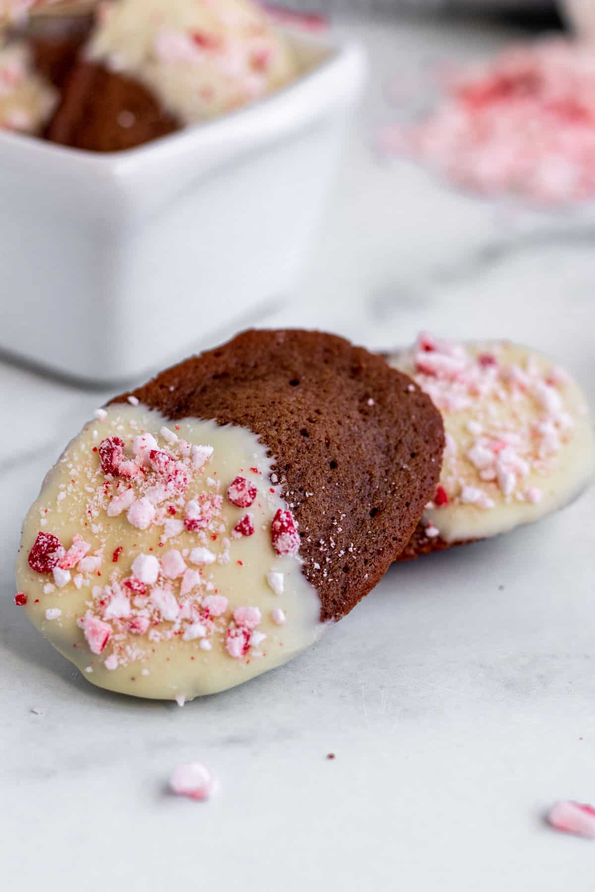 close up of a chocolate peppermint madeleines with a container of madeleines in the background