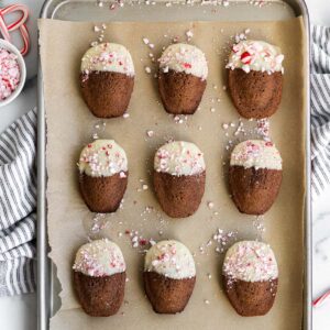 Cookie sheet with chocolate madeleines dipped in white chocolate and sprinkled with peppermint candies