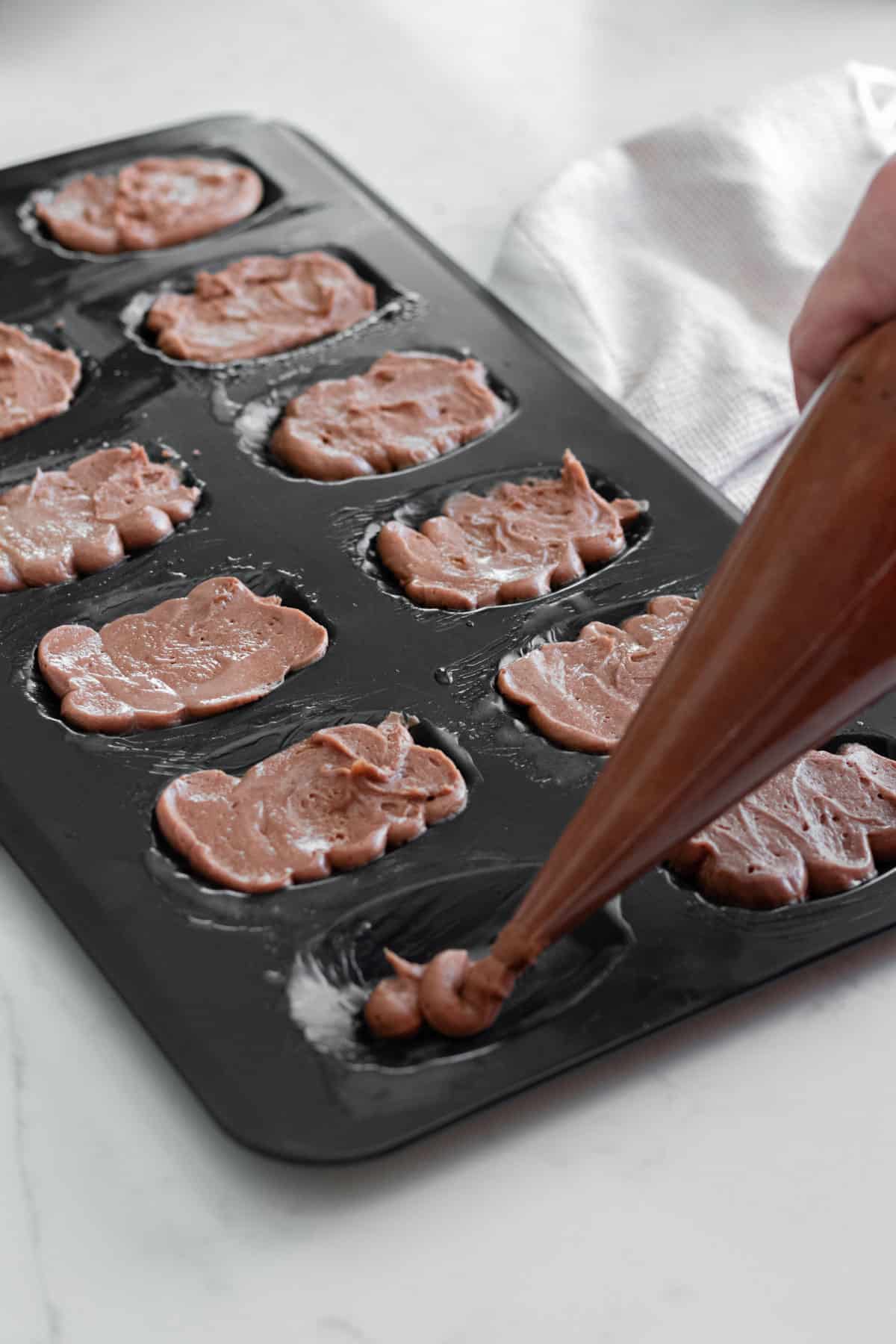 piping chocolate madeleine batter into a madeleine pan