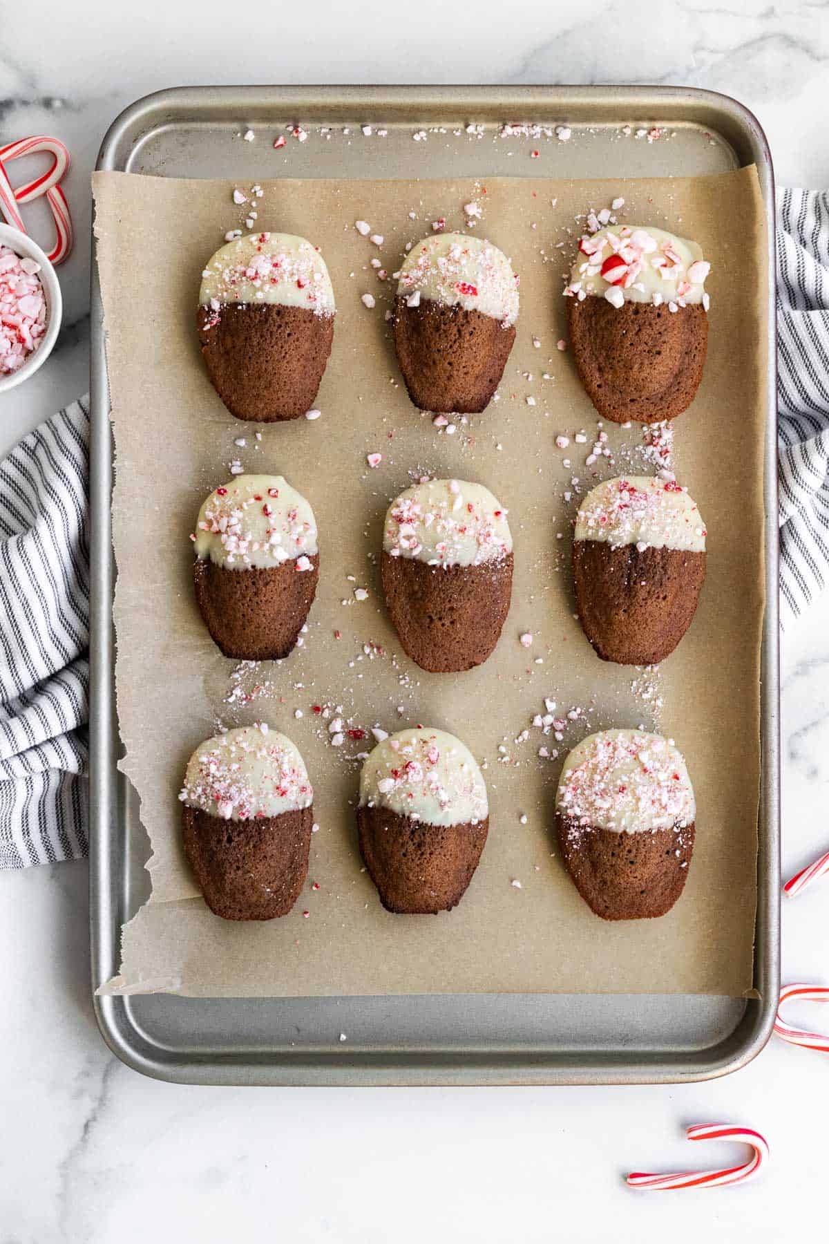 Cookie sheet with chocolate madeleines dipped in white chocolate and sprinkled with peppermint candies