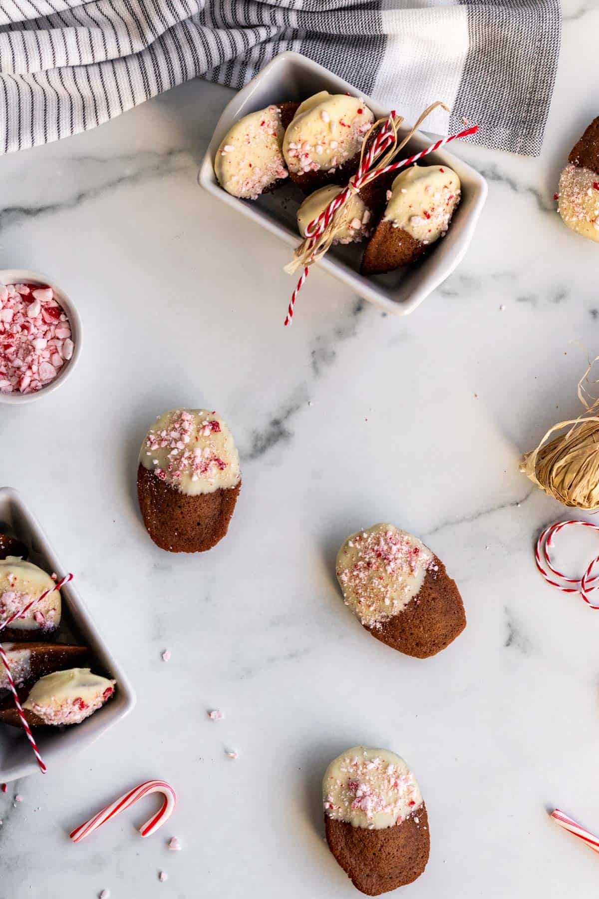 white containers of chocolate madeleines dipped in white chocolate and sprinkled with crushed peppermints sitting on a marble counter 