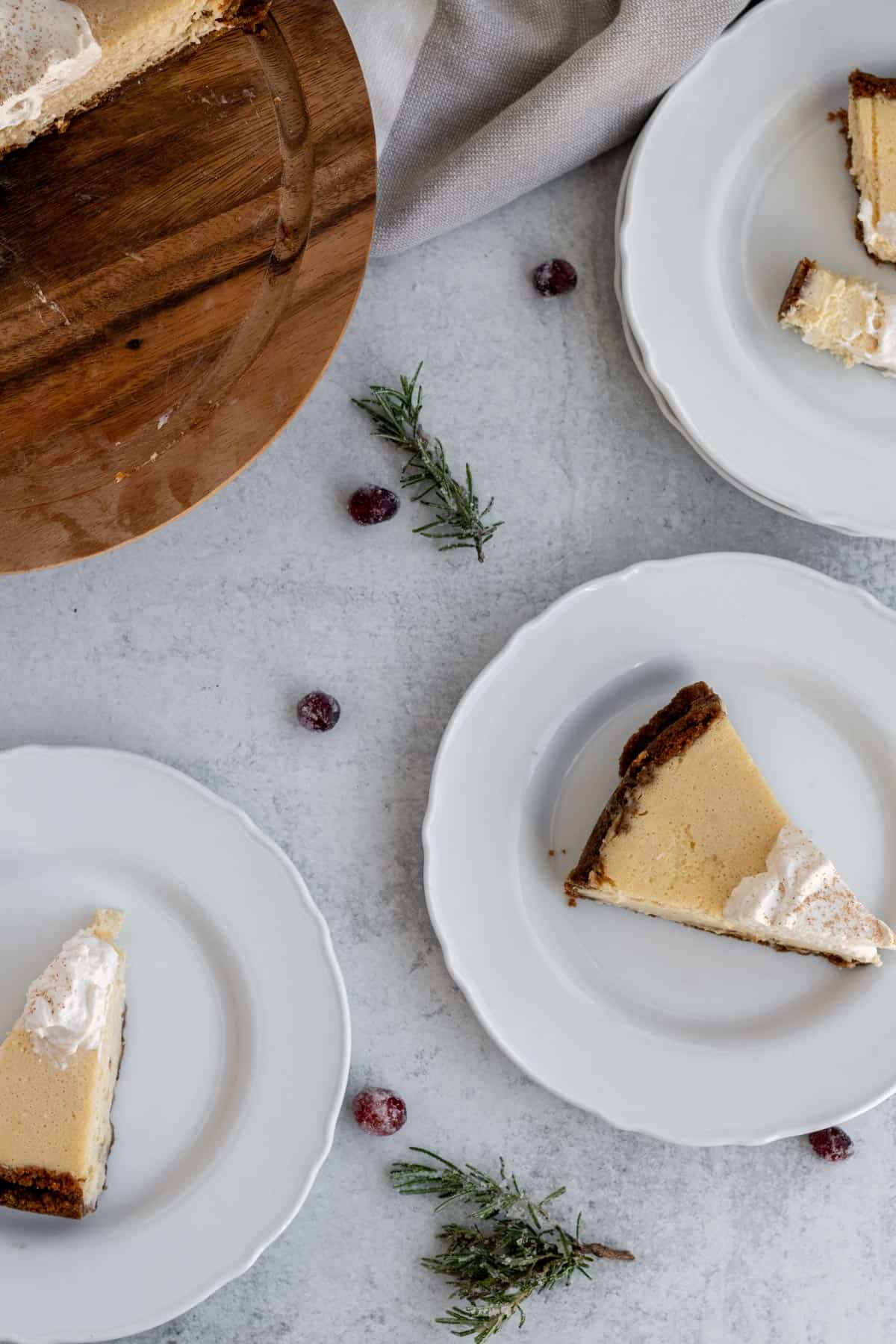 white plates with cheesecake slices on them and scattered rosemary sprigs and cranberries