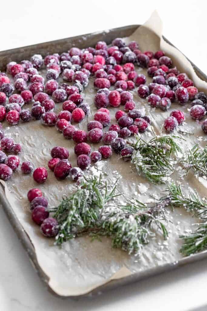 sugared cranberries and rosemary on a parchment lined baking tray