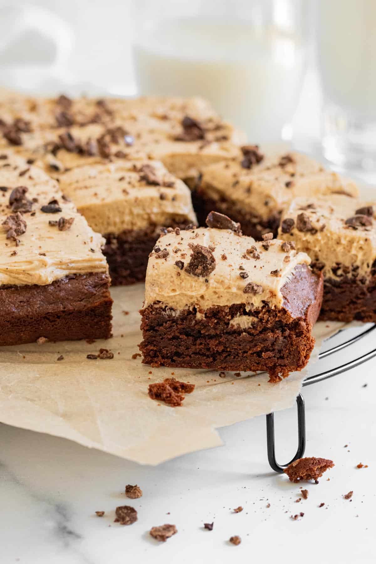 brownies with espresso frosting on top of a cooling rack with glasses of milk in background