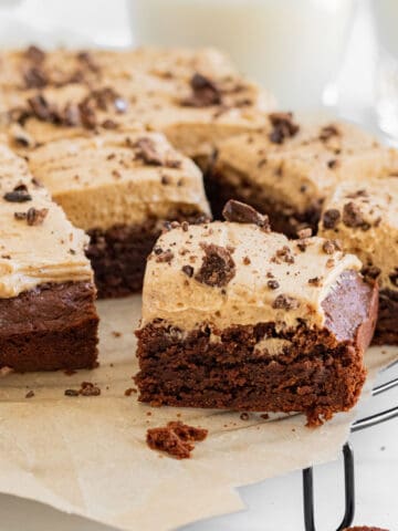 brownies with espresso frosting on top of a cooling rack with glasses of milk in background