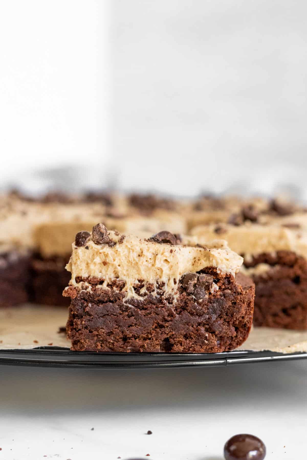 close up of a slice of brownie with espresso frosting on a cooling rack with other brownies in the background