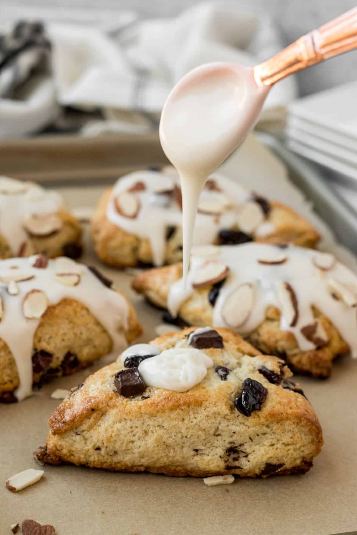 baking sheet of scones with a spoon dripping glaze onto a scone